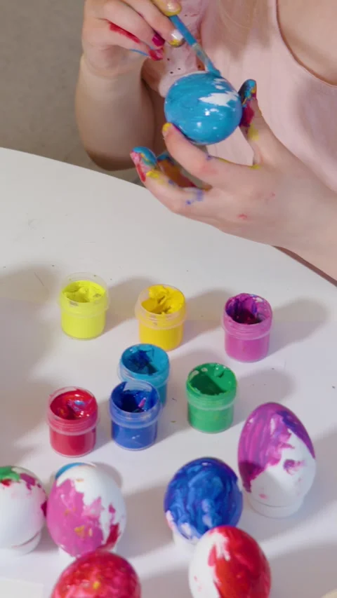 A child joyfully colors Easter eggs using various vibrant paints Stock Footage 302069433