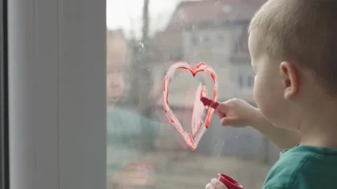 A Child is Joyfully Drawing a Heart on the Window Using Bright Red Paint and Video stock 307449510