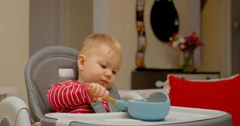 Child joyfully learns to eat alone during breakfast time at home Stock Photos