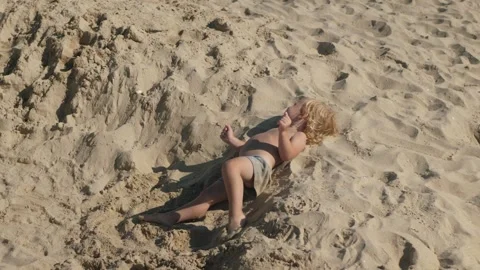 Child Joyfully Lying in Sand on Sunny Beach Stock Footage 303497686