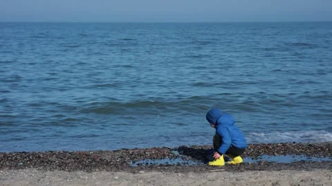 A Child is Joyfully Playing on the Beach While Wearing Bright Yellow Rain Boots Video stock 304730468