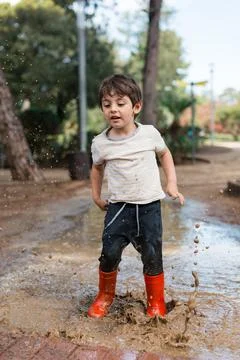 Child joyfully splashing in a muddy puddle Stock Photos