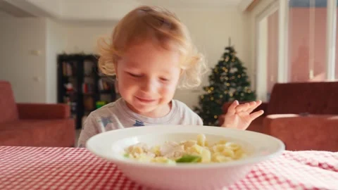The child in the kitchen at the table eating macaroni with ketchup. Mother adds Stock-Footage 228876401