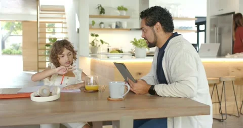 Child at kitchen table pausing with red pencil writing work while father Stock Footage 342023502