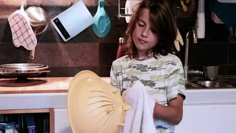 Child in the kitchen wiping with a cloth the items out of the dishwasher  Stock Footage 138437683