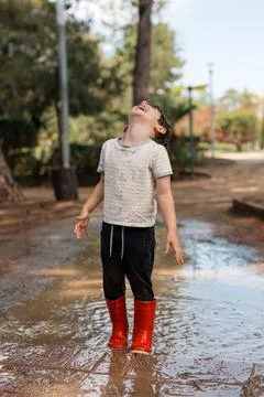 Child laughing playing in mud puddle wearing red boots Stock Photos