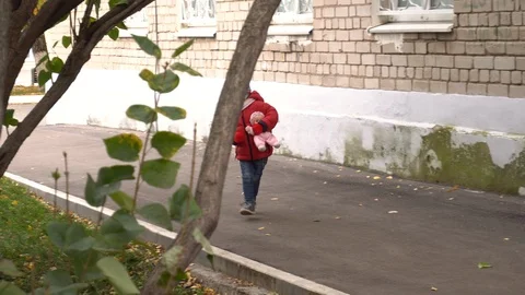 The child laughs and runs down the street with a doll in his hands. Little girl Stock Footage 118489356