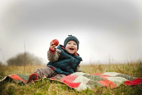 The child laughs at a picnic and eats a delicious apple Stock Photos