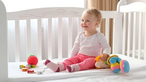 Child laughs sitting in a white bed among the toys. Stock Footage 126757957