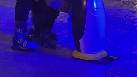 A child learning ice skating with a penguin trainer aid on a rink with purple Stock Footage 345665659