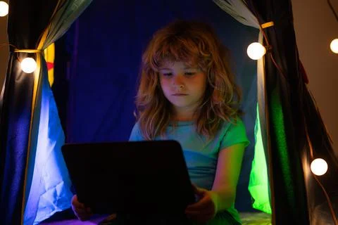 Child learning online at night, using laptop in living room at home. Stock Photos