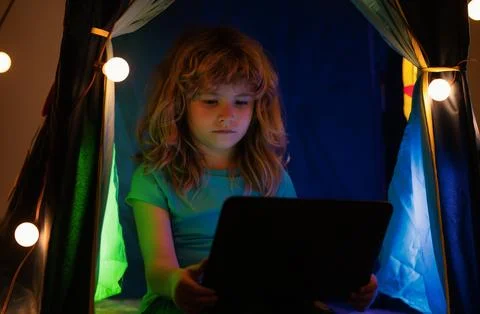 Child learning online at night, using laptop in living room at home. 스톡 사진
