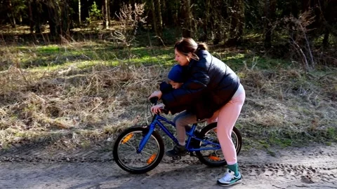 Child learning to ride a bicycle outdoors in a forest area during sunny weather Stock Footage 306440168