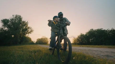 Child learning to ride a bike with the help of his father at sunset Stock Footage 245172148