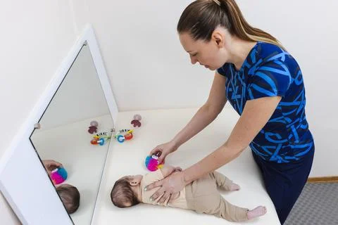 Child learning to roll over with guided support from physical therapist Stock Photos