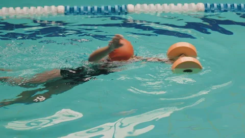 Child learning to swim in indoor pool using foam dumbbells, kids swimming lesson Stock Footage 326071477