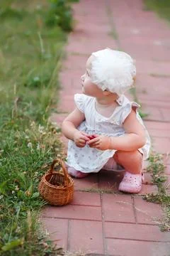 A child learning to walk sits on a path of slabs in the backyard of the house Stock Photos