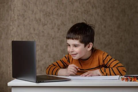 The child learns remotely through the computer. The boy draws with pencils and Stock Photos