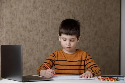 The child learns remotely through the computer. The boy draws with pencils and Stock Photos