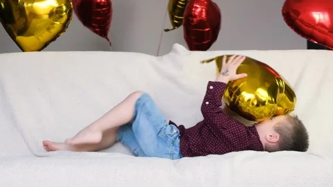 Child, lies on a light sofa and plays with a balloon in the form of a heart Stock Footage 146163447