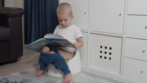 Child little boy leafing through a children picture book sitting on potty Stock Footage 263704982