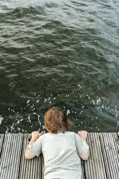 Child Looking Down at Dark Water from Wooden Dock 스톡 사진