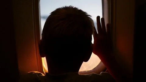 A child looking out the window of an airplane at sunset Stock Footage