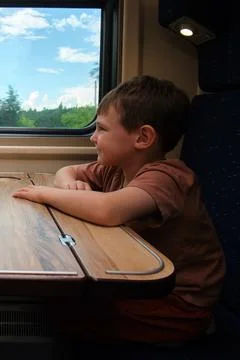 Child looking out window inside train. Little boy sitting at table during tra Stock Photos