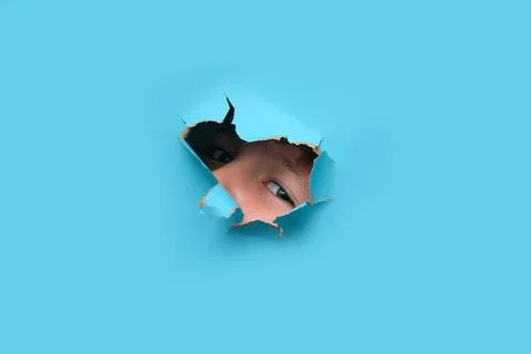 Child looking through hole in blue paper, copy space. Curious boy peeking wit Stock Photos