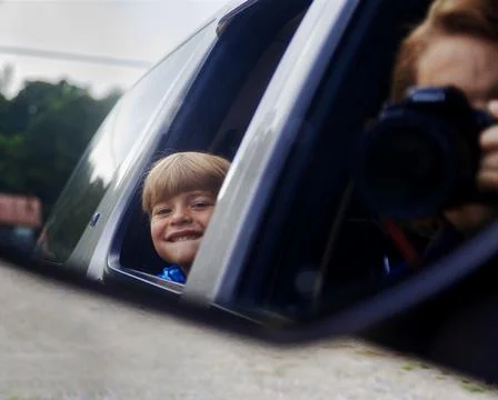 Child looking through window and woman snaps a picture from front seat. Foto stock