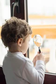Child looking through a window through a magnifying glass Stock Photos
