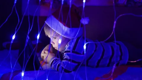 The child looks to the tablet lying on bed in hat santa.On the foreground 動画素材 70839618