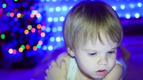 The child looks to the tablet lying on bed. In the background, lights and Vidéo 71010302