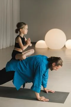 A child in the lotus position sits on the back of a yoga coach during trainin Foto stock
