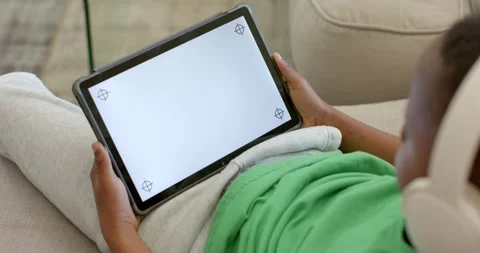 Child is lying back on pale couch, shifting for comfort, tilting tablet and Stock Footage 336609415
