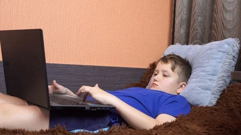 The child is lying on the bed and playing on the laptop. Clicks on the keyboard. Stock Footage 99045325