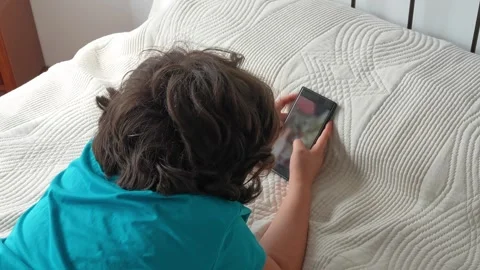 Child lying in bed using a smartphone Stock Footage 341599396