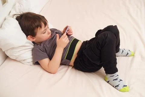 Child lying on a bed using a smartphone. Indoor lifestyle photography with ca Foto stock