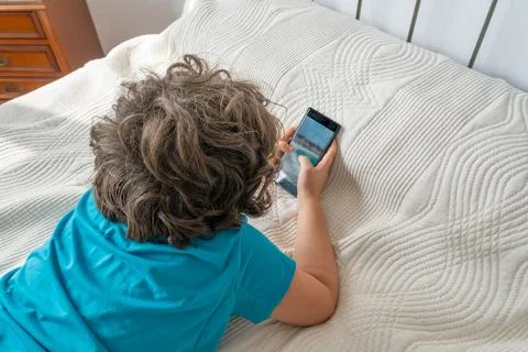Child lying on bed using smartphone Stock Photos