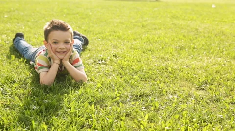 Child lying down on the grass portrait at town park in summer day Видео 64530674