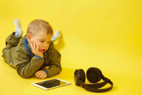 A child lying down uses a digital tablet on a yellow background Stock Photos