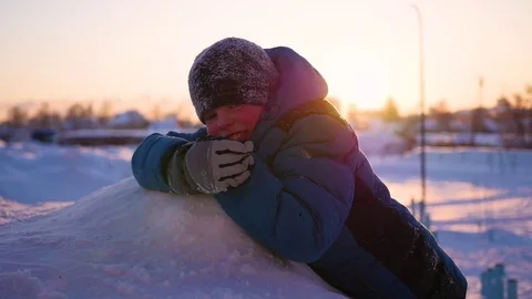 The child is lying on snow and looking at the sunset. winter Park 库存影片 71982593