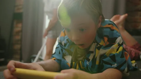 Child is lying on the sofa and playing on the phone while mom vacuums apartment Stock Footage 233777421