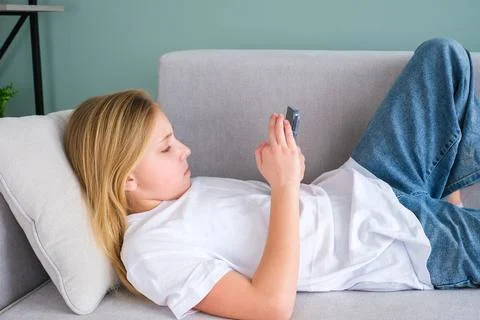 The child is lying on the sofa and using the phone. Stock Photos