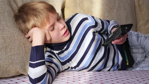 The child is lying on the sofa with the TV remote Video stock 69854660