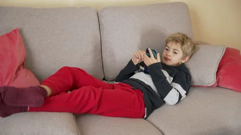 Child lying on the sofa watching video or photo content in social network Stock Footage 239373840