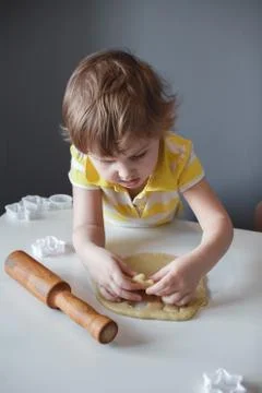 The child makes cookie molds on a white table. Preparation of homemade desser Stock Photos