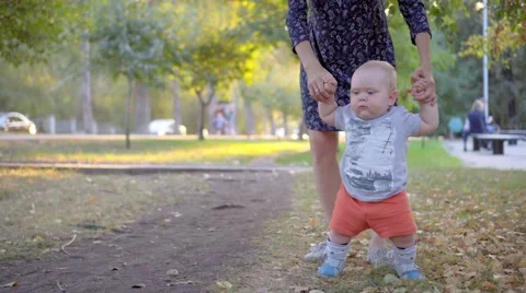 The child makes the first steps, mother help him. Autumn park Stock Footage 68811037