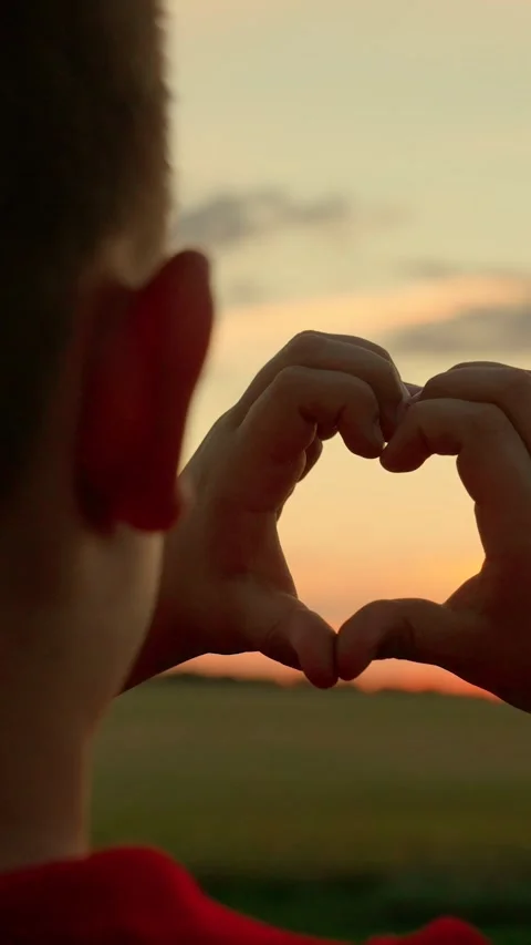 Child makes heart shape with his fingers against sunset. Child boy plays sun in Stock Footage 267660697