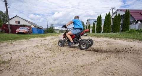 A child makes a sharp turn on an ATV, kicking up dust and sand from the road Stock Photos